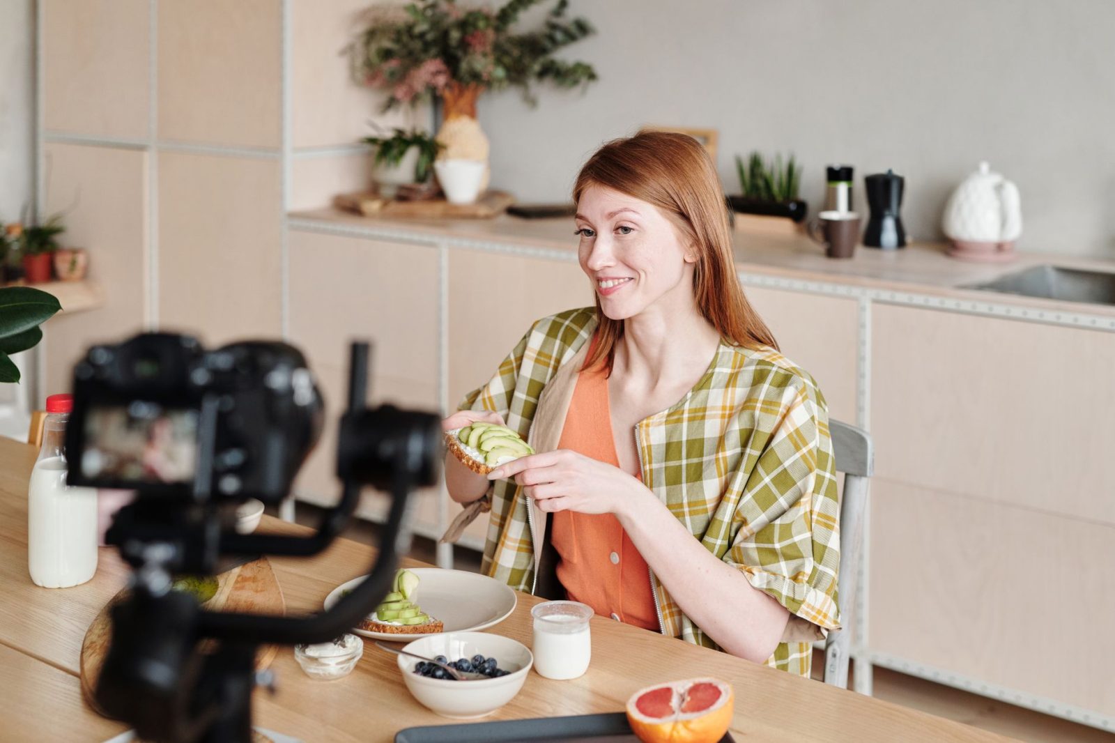 Lächelnde Frau filmt einen Vlog über die Zubereitung von Avocado-Toast zu Hause.